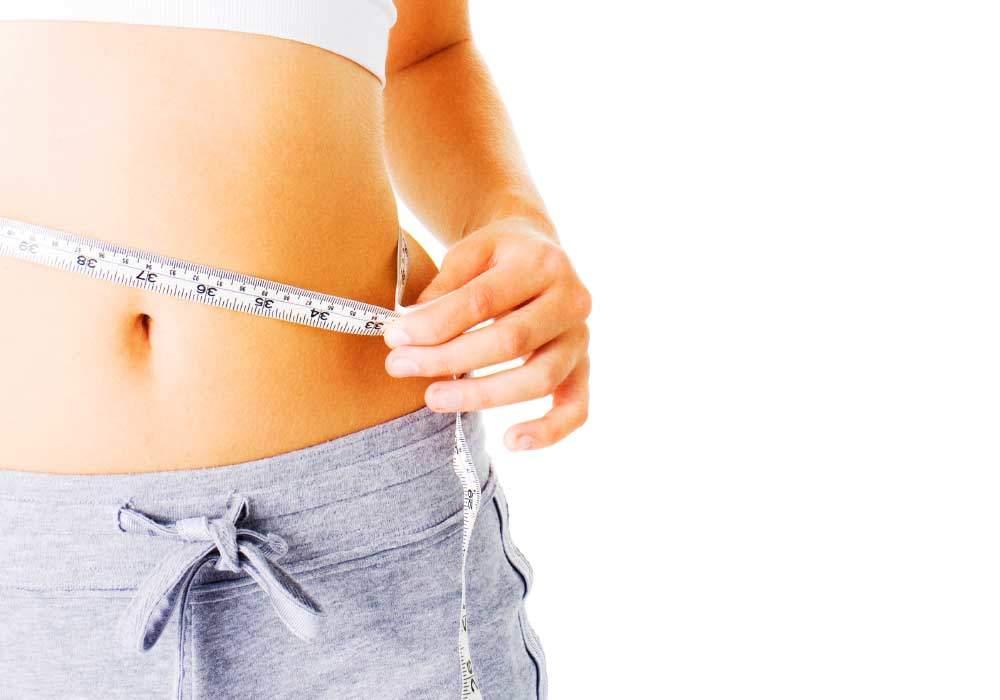 a woman measuring her waist after undergoing a phycian prescribed weight loss program
