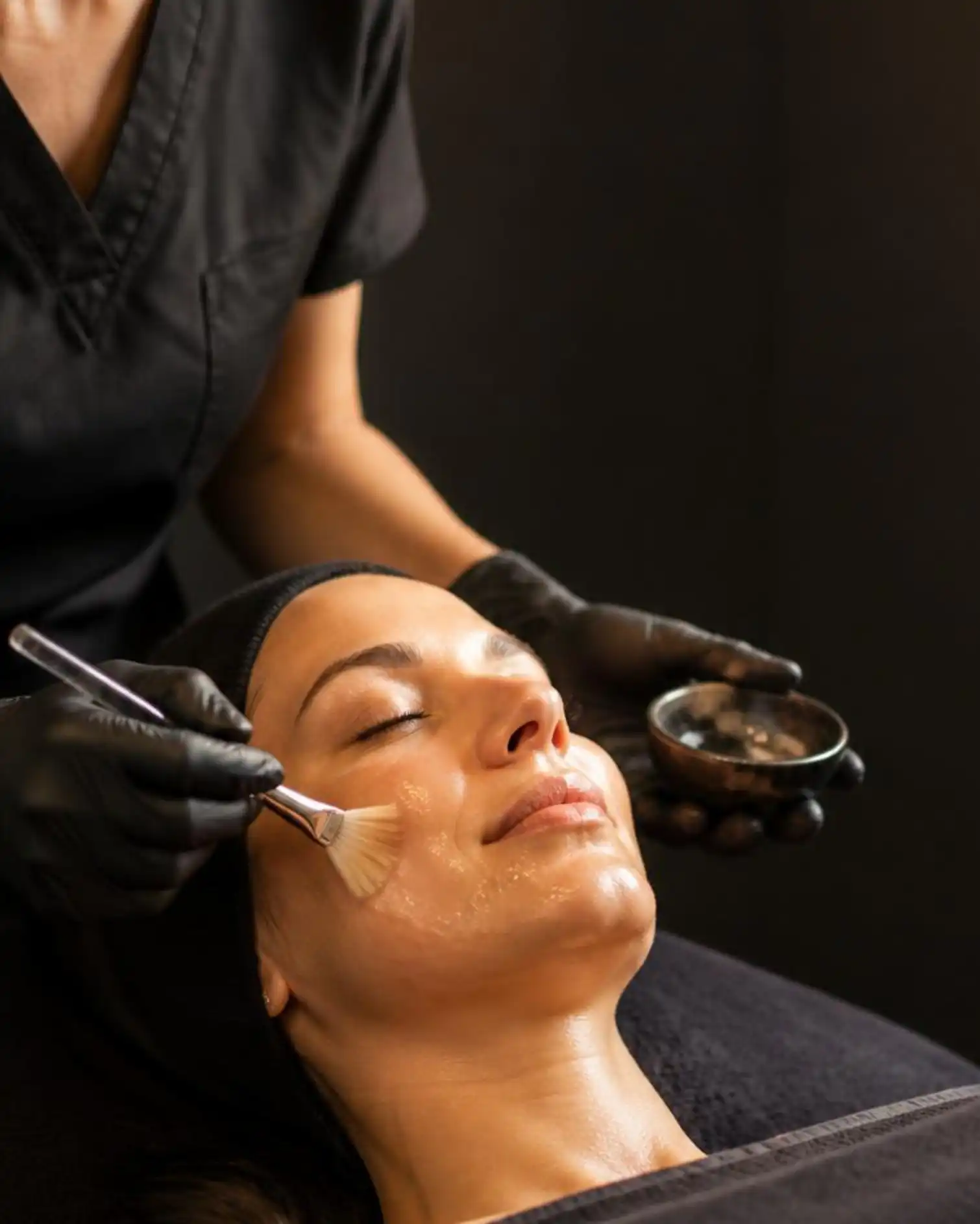 Licensed esthetician in black scrubs applying a custom facial treatment with a brush to a client's cheek at Beau Visage Aesthetics in Walnut Creek