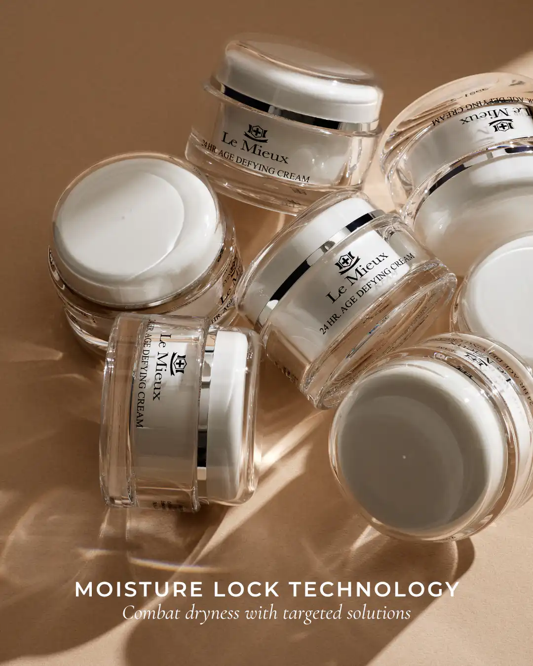 Several jars of Le Mieux 24 HR Age Defying Cream lying on a sandy beige surface in warm light